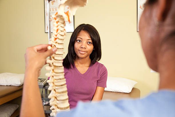 Chiropractic practitioner explaining spinal anatomy model to a patient in a clinic setting.