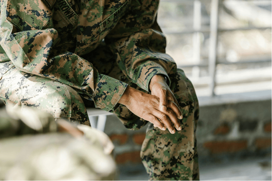 A soldier sitting with poor posture, potentially experiencing back pain or spinal stress.