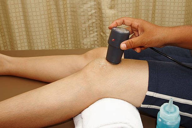 A chiropractor applying ultrasound therapy to a patient's knee joint during a treatment session.