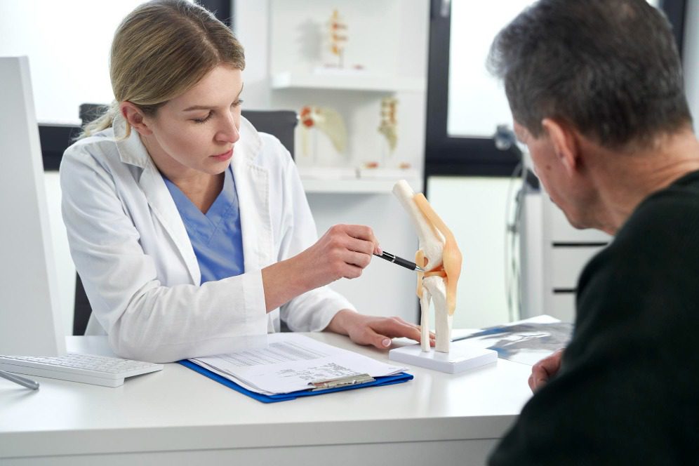 A chiropractor discusses knee joint health using an anatomical model with a patient during a consultation.
