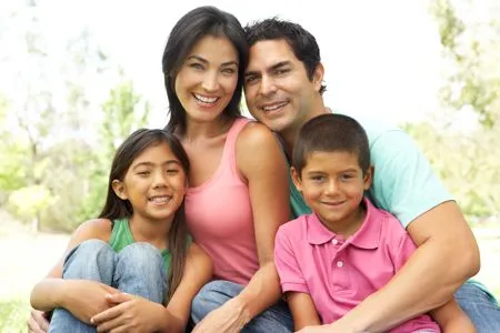 A happy family of four, including a mother, father, daughter, and son, smiling outdoors.