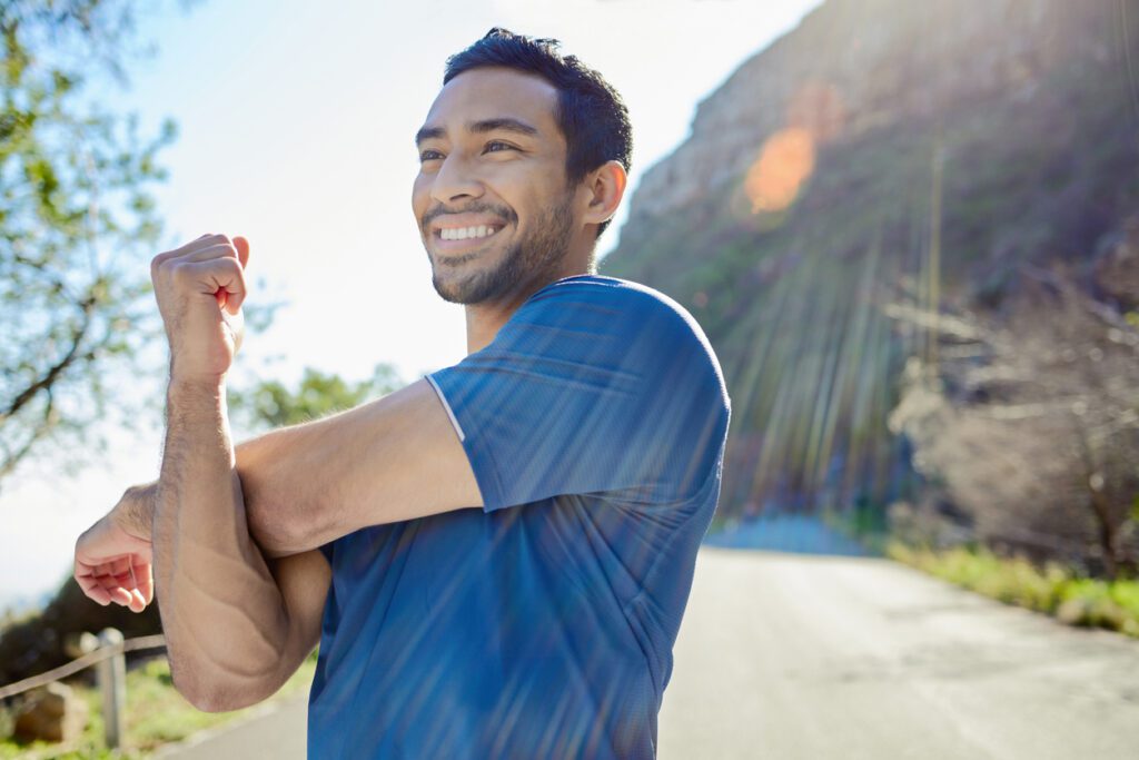A smiling man with a beard stretching his arm.