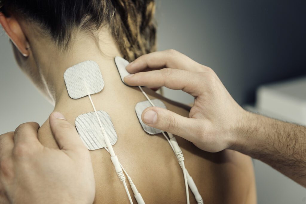 Close-up of a patient’s upper back and neck as a physical therapist applies TENS or electrotherapy treatment.