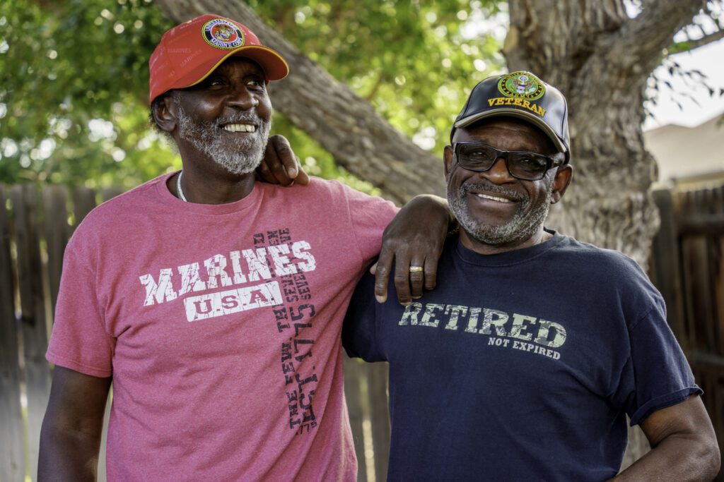 Two senior African American military veterans embracing and smiling outdoors.