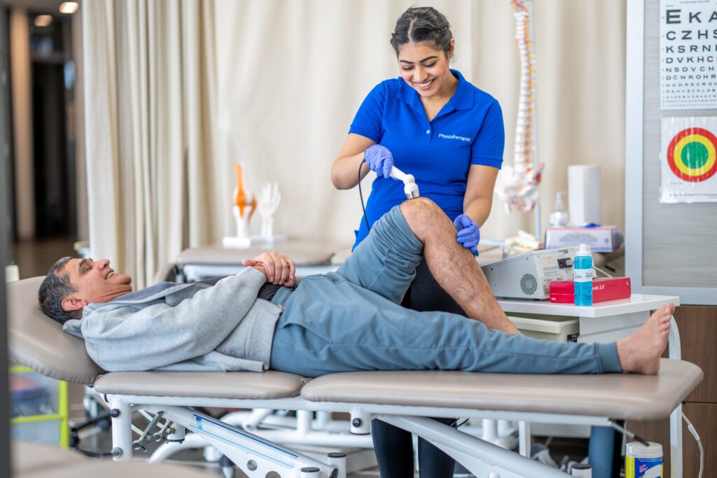 A chiropractor uses an ultrasound machine on a male patient's knee during a physical therapy session.