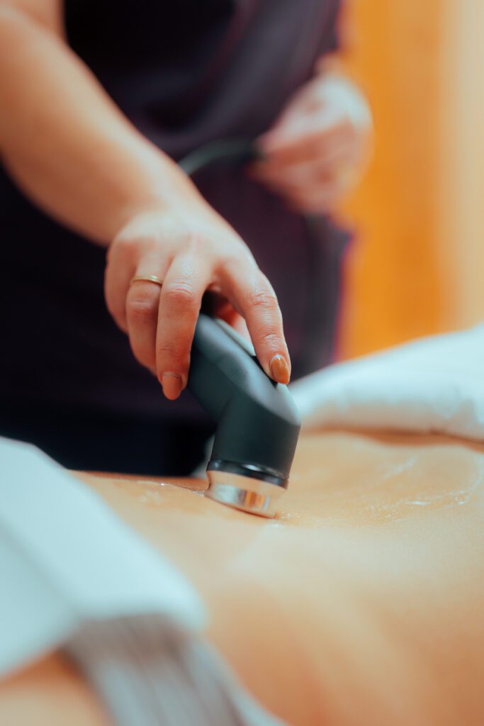 A chiropractor performs therapeutic ultrasound on a patient’s back using a specialized medical device.